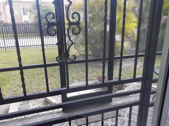 View from behind a decorative metal gate, showing a grass lawn and palm trees.