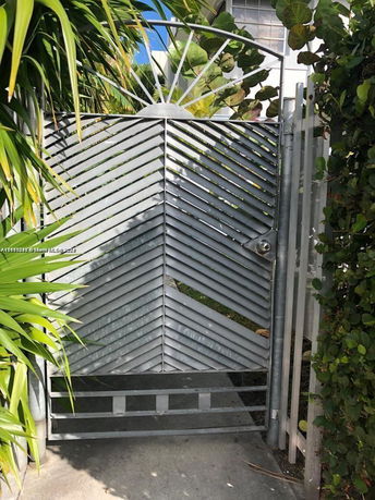 Exterior view of a metal gate with a decorative pattern, surrounded by greenery.
