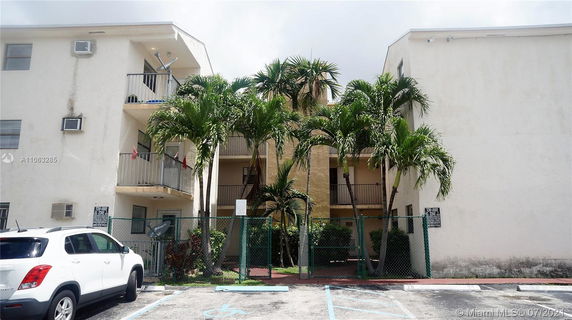Front view of a multi-story apartment building with balconies and a parking area.