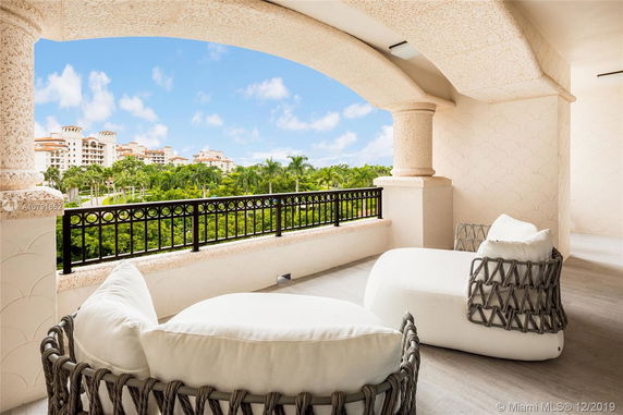 View from a balcony with outdoor seating, overlooking lush greenery and adjacent buildings.