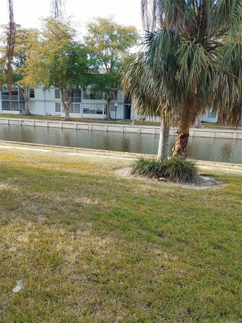 View of a canal and grassy area in front of a building with trees.