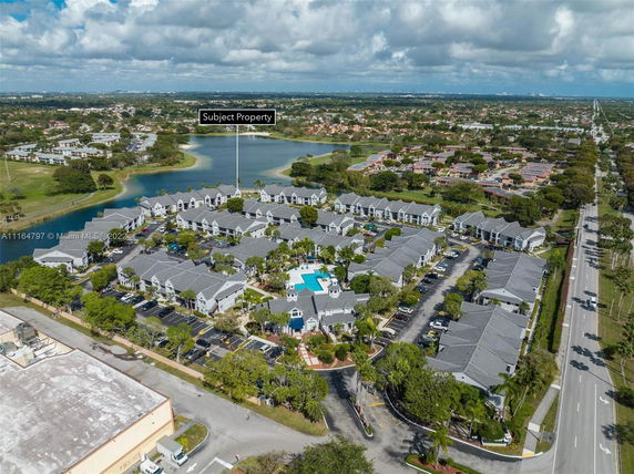 Aerial view of residential complex near a lake with surrounding roads and greenery.