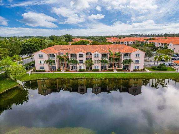 View of a residential building complex with red-tiled roofs by a water body.