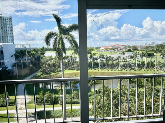 Panoramic view from a balcony showing palm trees, water, and distant buildings under a blue sky.