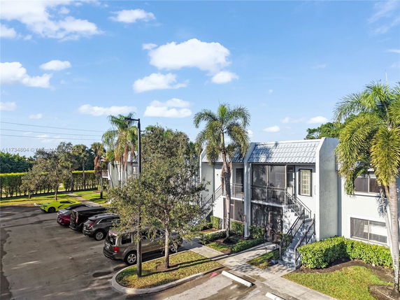 View of a residential building with a parking area and palm trees.