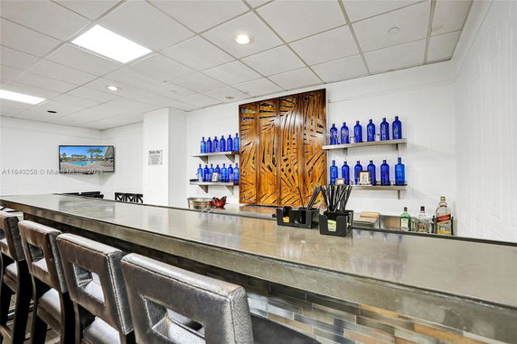 Indoor bar area with stools, shelves of blue bottles, and a decorative wooden panel.