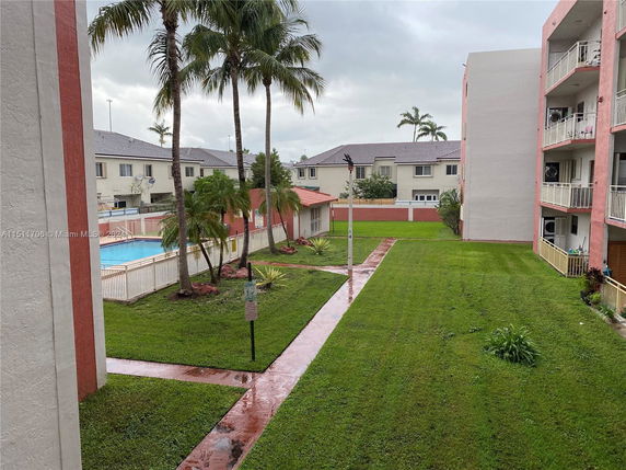 View of an apartment complex with balconies and grassy areas leading to a swimming pool.