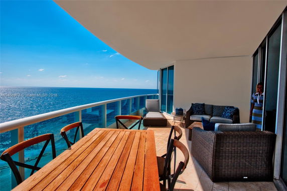 Balcony view of the ocean with outdoor furniture and glass railing.