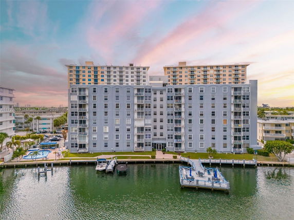 Front view of a multi-story apartment building along a waterfront with a dock and boats.