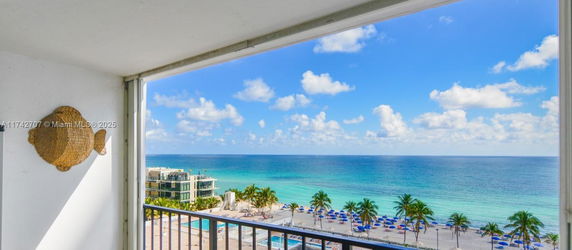 Scenic view of the sea and beach with umbrellas and palm trees captured from a building.