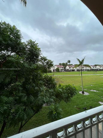 View from a balcony overlooking a grassy area with trees and neighboring houses in the distance.