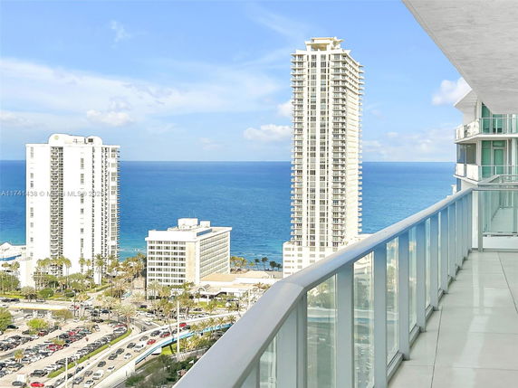 Panoramic view from a high-rise building balcony overlooking the ocean and nearby skyscrapers.