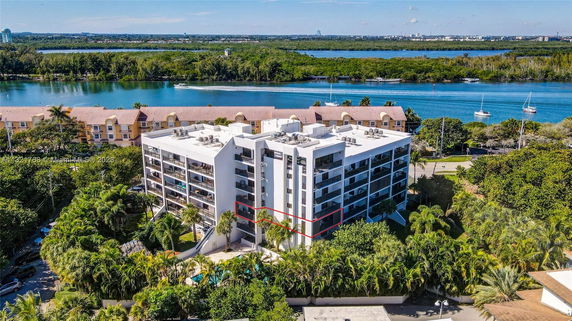 View of a multi-story building near a body of water and surrounded by trees.