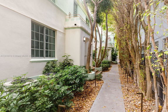Side view of a building with a walkway lined with trees and plants.