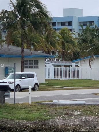 View of a small building with a pitched roof and surrounding palm trees.
