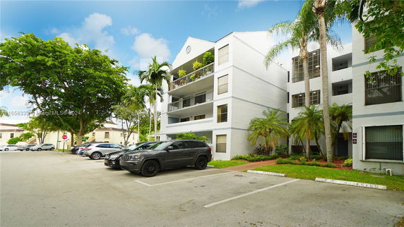 Exterior view of a multi-story residential building with a parking area in front.