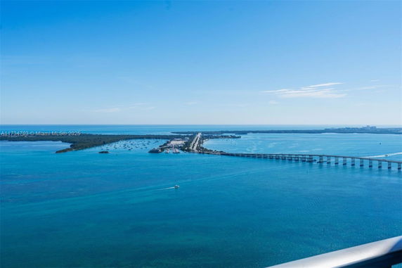 Panoramic view of a bridge over a large body of water with distant landmass and clear blue sky.