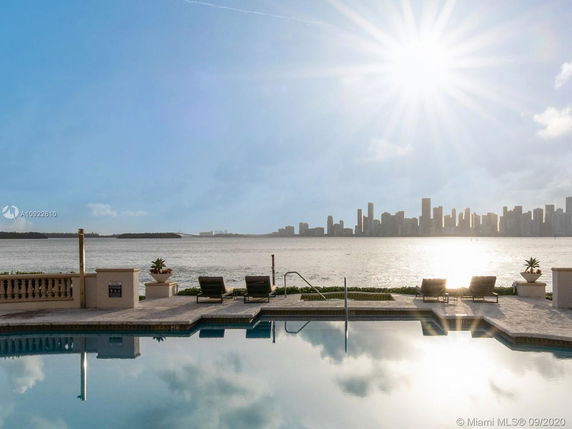 View of a waterfront with a pool in the foreground and city skyline in the background.
