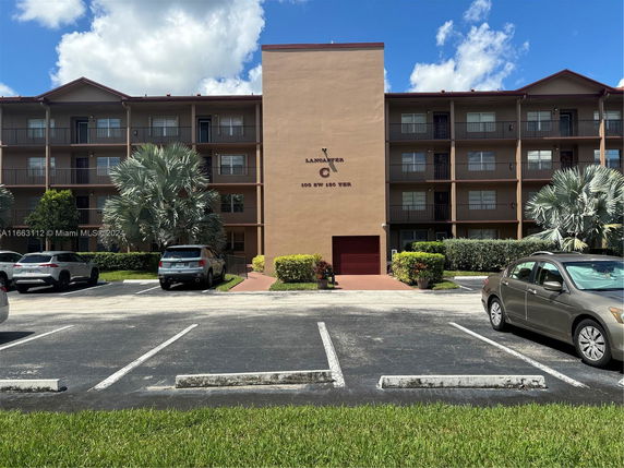 Front view of a multi-story apartment building with parking spaces.