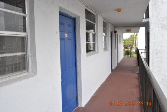 Outdoor walkway with blue doors and windows on a white building.