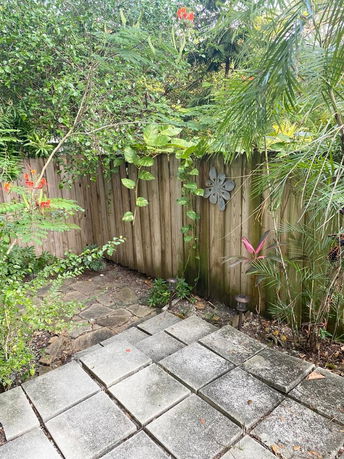 Outdoor area with stone-tiled steps leading to a wooden fence surrounded by lush greenery.