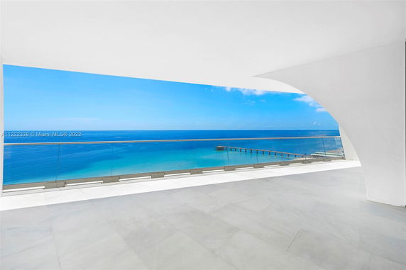 Wide angle view of the ocean from a balcony with glass railing.