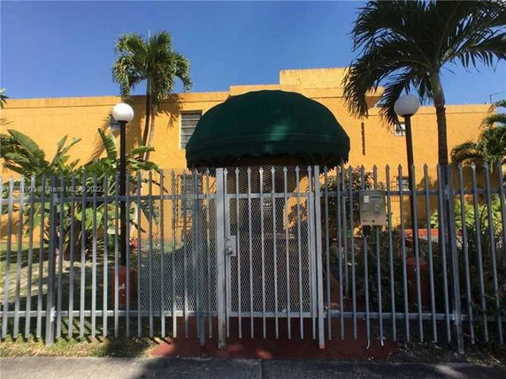 Front view of a yellow building with a green canopy entrance and surrounding fence.