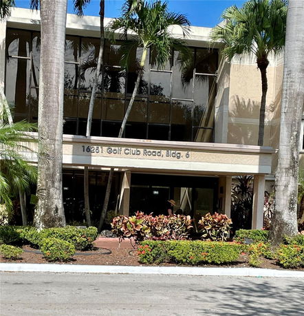 Front view of a multi-story building with glass windows and surrounded by palm trees.
