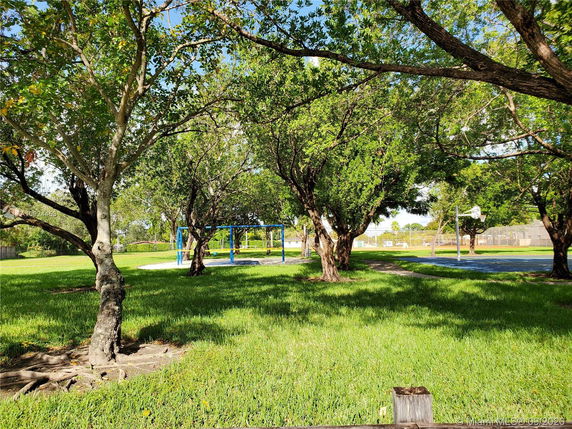 Playground with swing set and basketball court surrounded by trees and grass.
