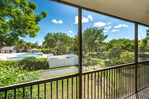 View from a screened balcony overlooking a pool and lush greenery.