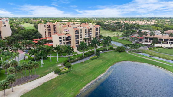 Aerial view of a multi-story residential building complex with surrounding landscaped greenery and a body of water.