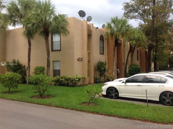 Front view of a two-story building with beige exterior and several windows, surrounded by palm trees.