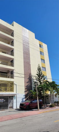 Front view of a multi-story residential building with balconies and a parked car at the entrance.