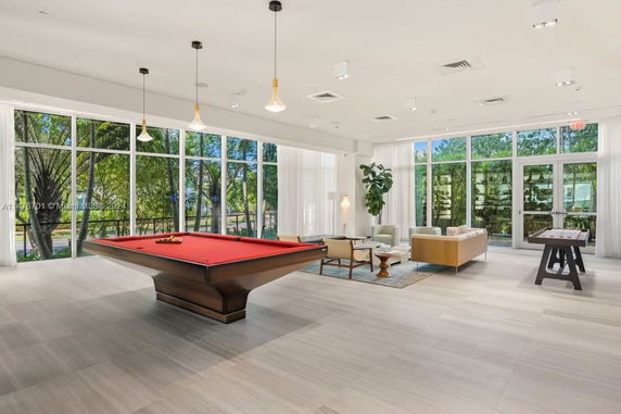 Interior view of a recreation area with a pool table and seating, featuring large windows.