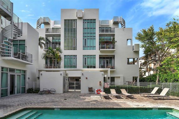 Modern multi-story building with large windows and balconies near a swimming pool.