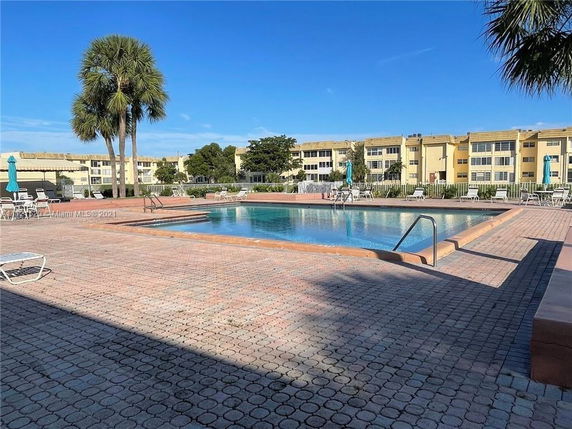 Outdoor swimming pool with surrounding patio and buildings in the background.