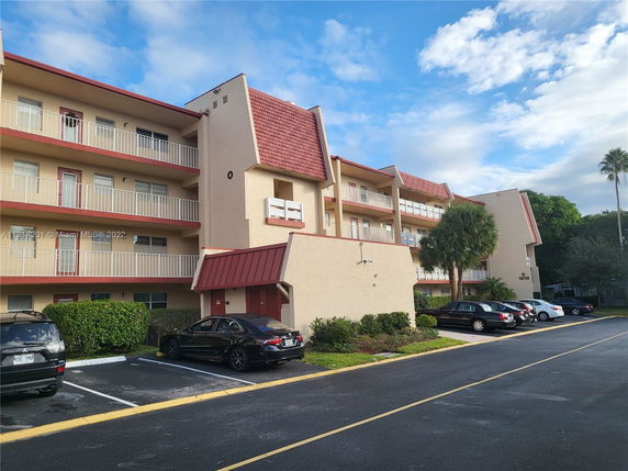 Front view of a multi-story apartment building with balconies and parking area.