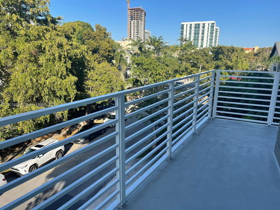 View from a balcony overlooking trees and a city street with buildings in the background.