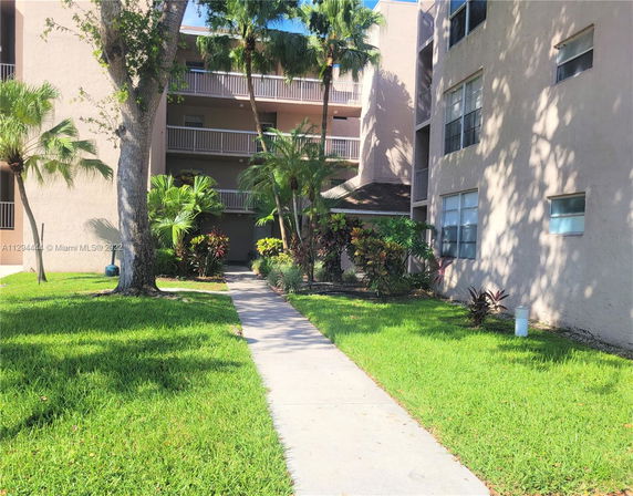 Front view of a multi-story residential building with balconies and surrounding greenery.