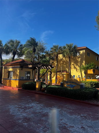 Front view of a building with yellow walls and a red-tiled roof surrounded by palm trees.