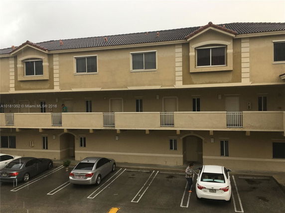 Front view of a multi-story apartment building with covered balconies and parking spaces below.