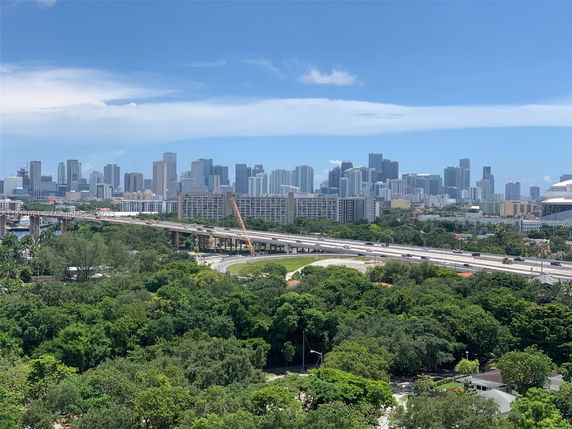 Wide angle view of a city skyline with lush greenery and highways in the foreground.