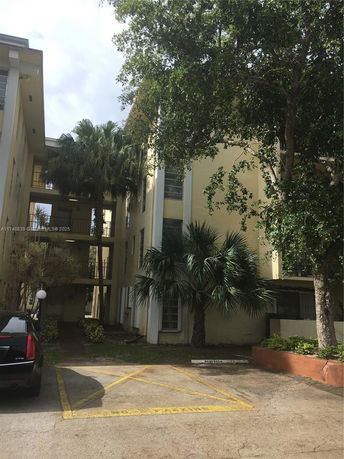 Front view of a multi-story apartment building with trees and a parking area in front.