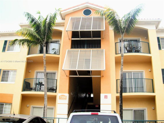 Front view of a multi-story apartment building with balconies and palm trees.