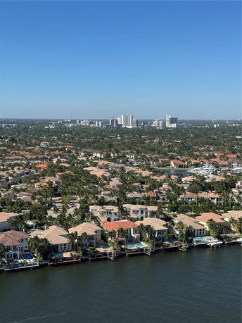 Aerial view of a neighborhood with waterfront homes, greenery, and distant city buildings.