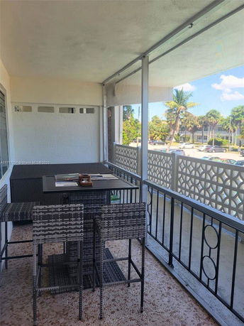 Outdoor balcony area with table and chairs and a view of nearby trees and buildings.