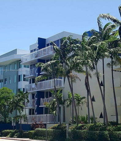 Front view of a multi-story apartment building with balconies and palm trees.