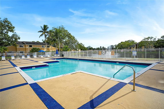 Outdoor swimming pool with surrounding lounge chairs and a safety fence.