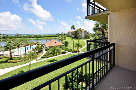 Balcony view overlooking a landscaped garden, pool, and distant ocean.