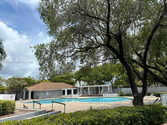 Outdoor swimming pool area with surrounding trees and a small building nearby.